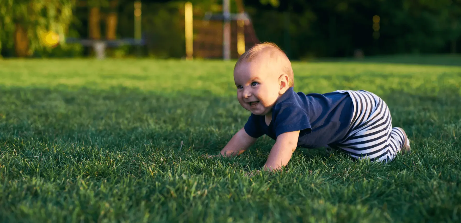 A baby crawling on the grass in a park.